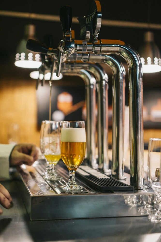 Beer pouring from the chrome tap tower into a glass on the bar, two glasses already filled.