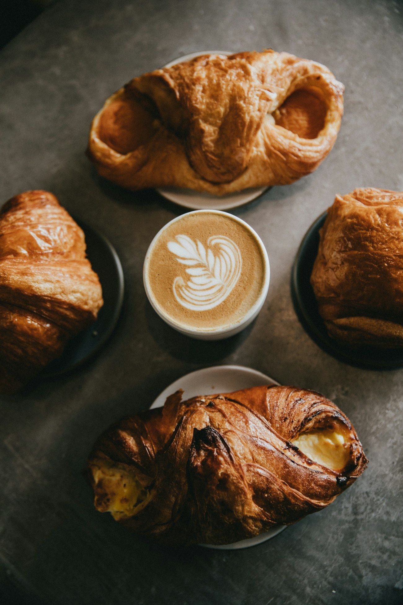 Flaky croissants on plates around a cup of coffee with latte art