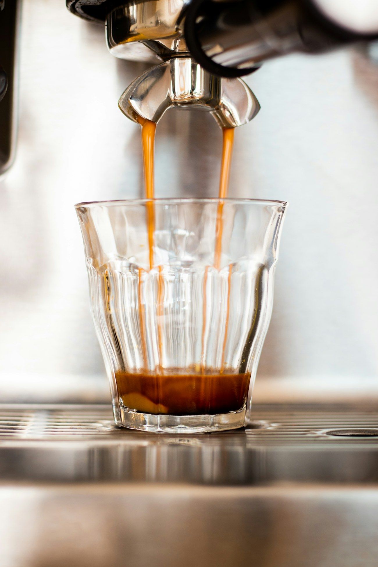 Amber espresso streaming from the machine into a small glass in soft morning light