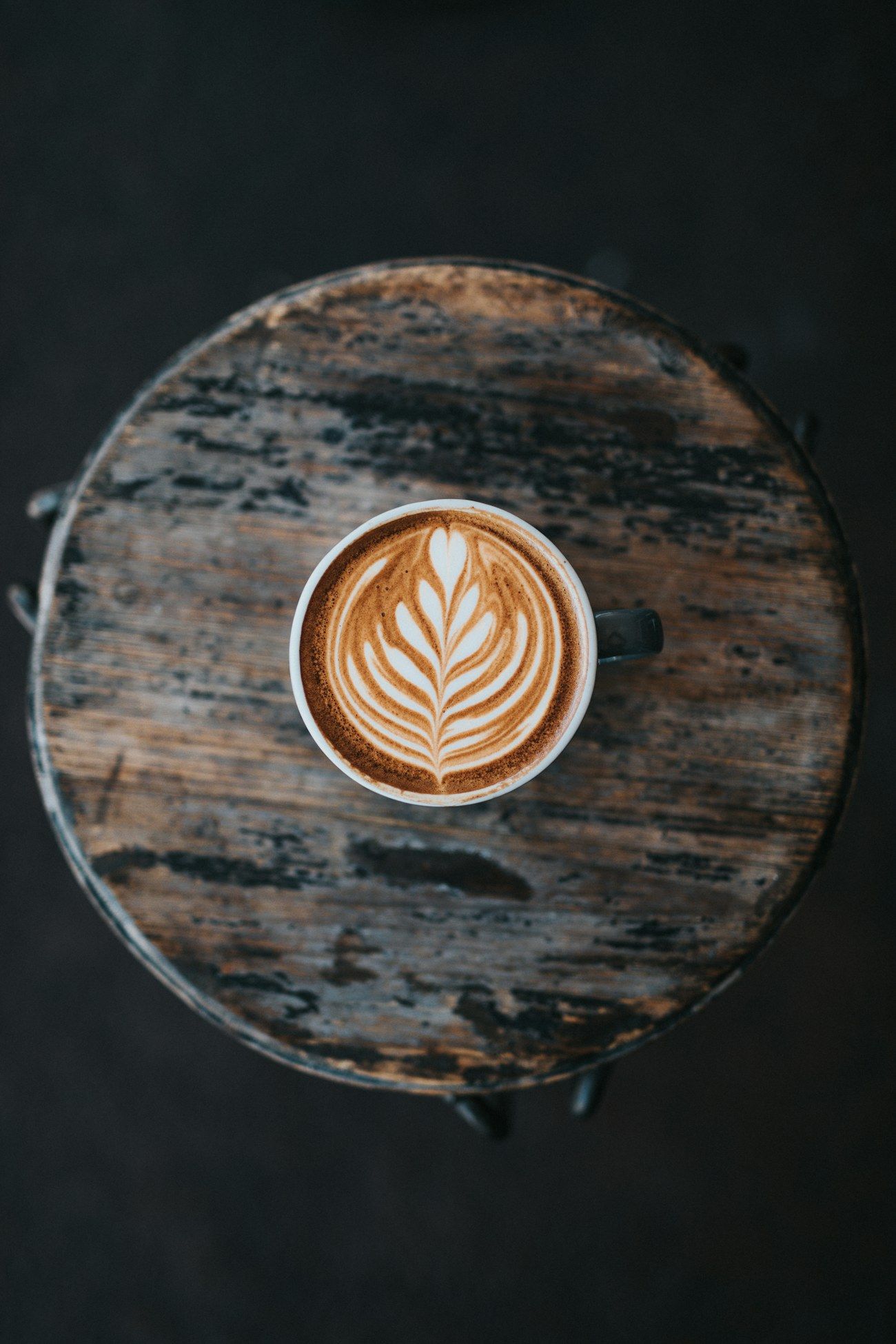 Latte art in a cup on a dark wooden table in moody, low dusk light