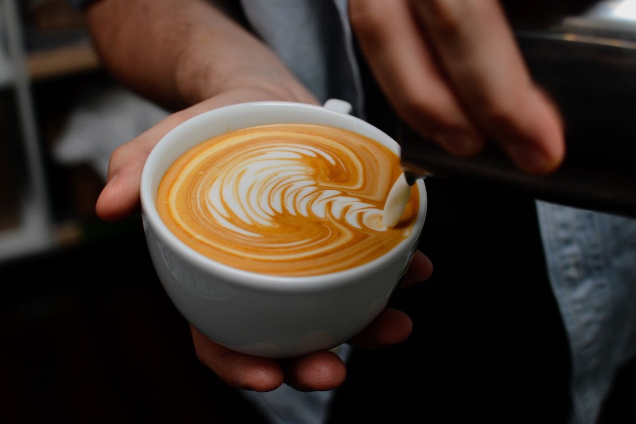 A cup of coffee with latte art cradled in one hand in warm, low evening light
