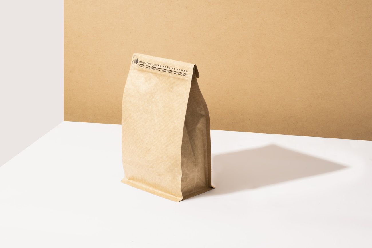 A kraft bag of coffee standing on a white surface against a tan backdrop