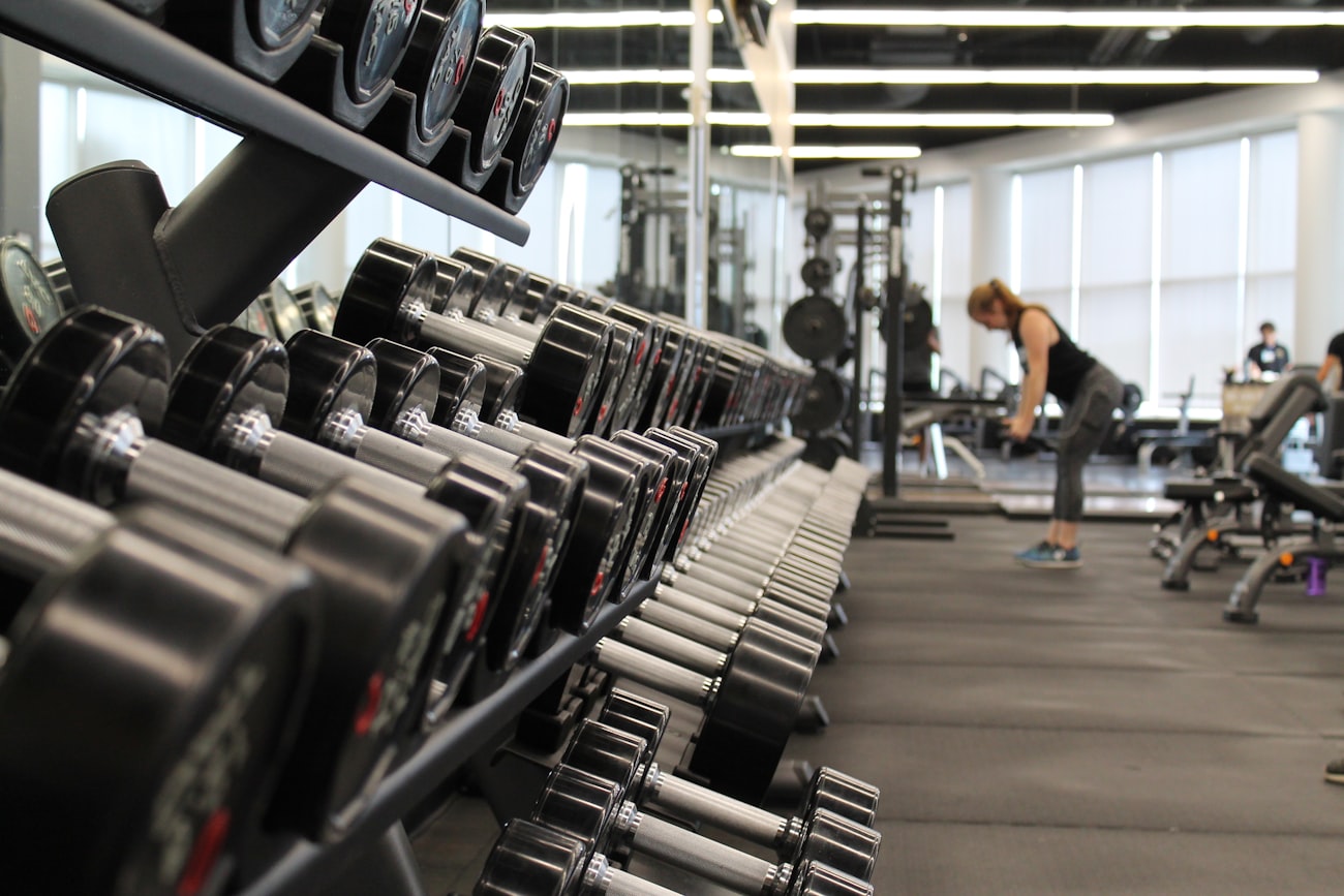 The gym floor at a fitness studio, weights racked, someone mid-workout
