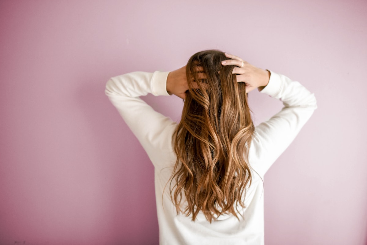 Someone running their hands through long, freshly colored hair against a soft pink wall.