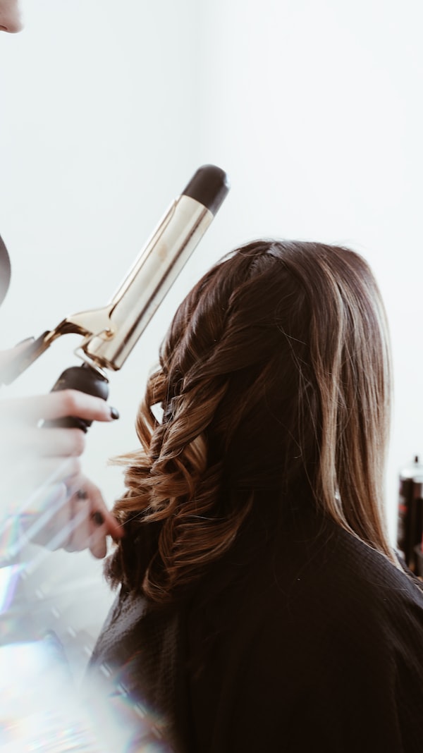 A stylist setting curls into long hair with a gold-barrel iron.