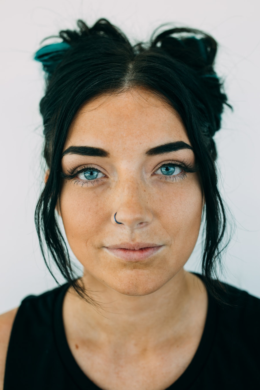 A stylist with dark hair pulled up, looking at the camera in soft studio light.