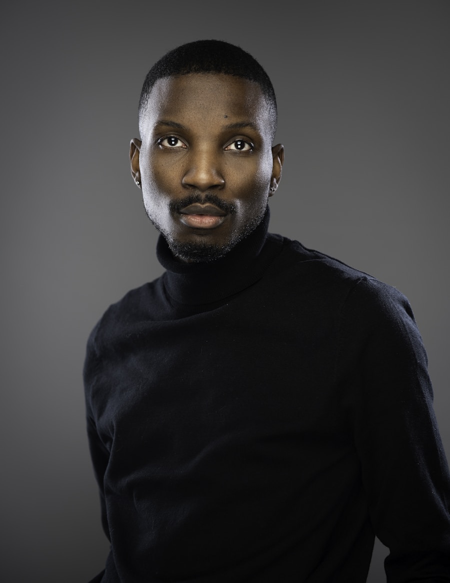 A stylist in a dark turtleneck, looking at the camera against a soft grey studio backdrop.