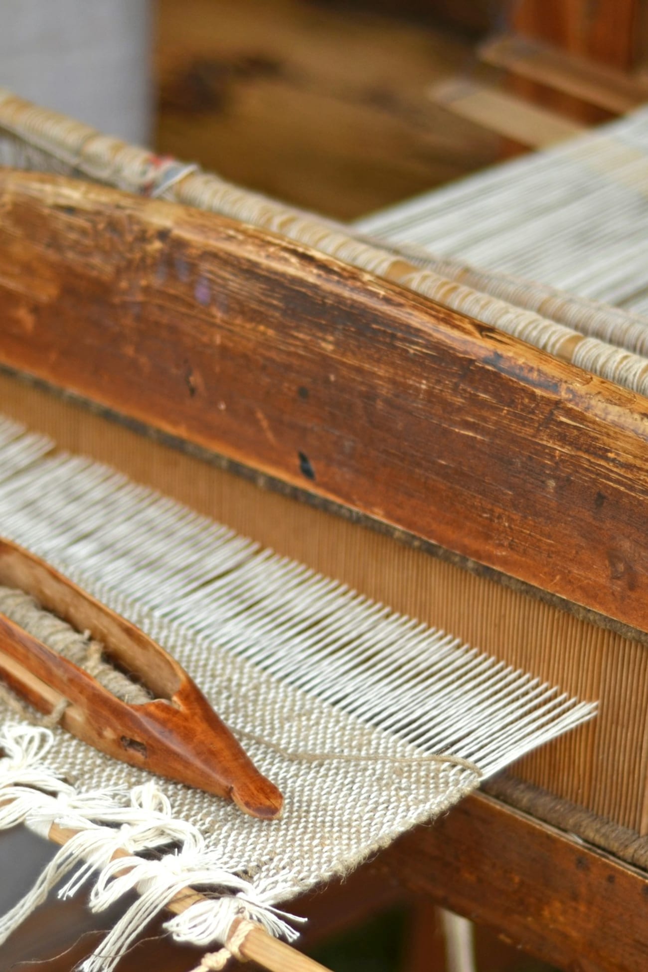 A wooden weaving loom with a shuttle and natural cream threads in the studio