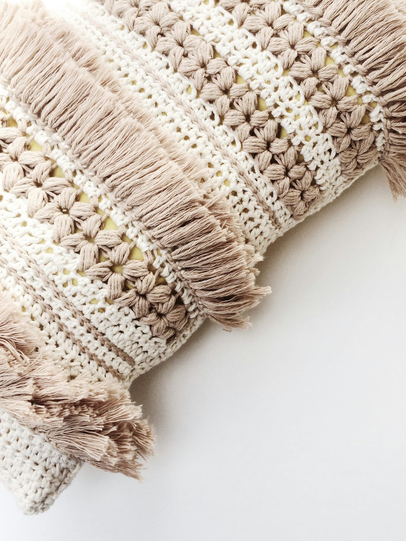 A handmade cream blanket with a fringed, knotted edge