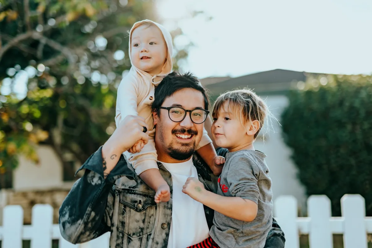 A parent outdoors with two young children, all looking toward the camera