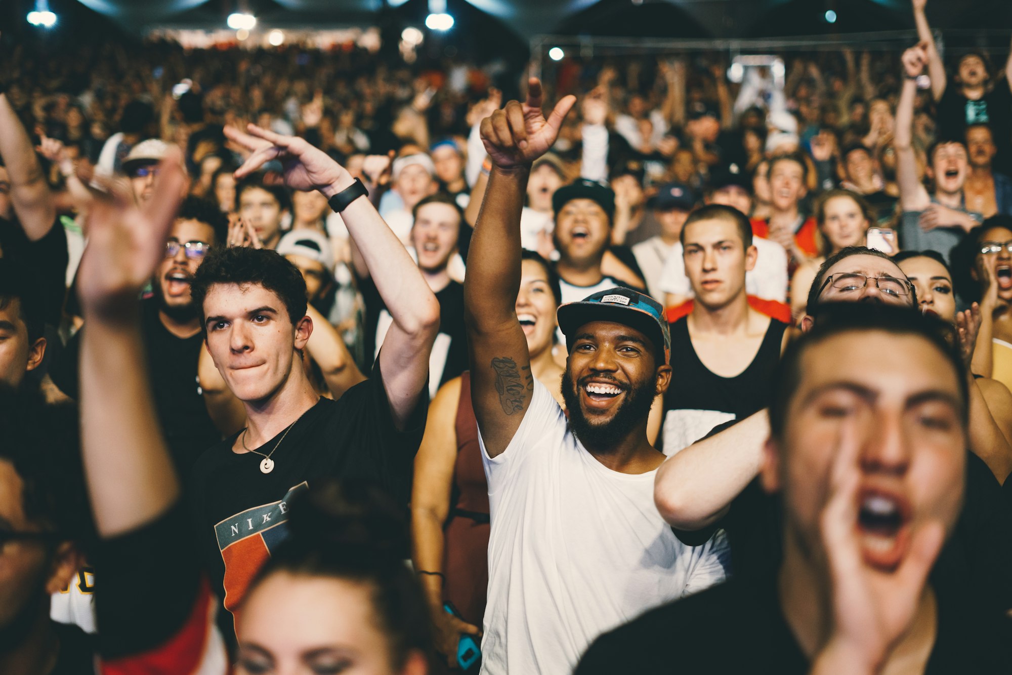 A crowd at a show, faces lit, hands raised toward the stage